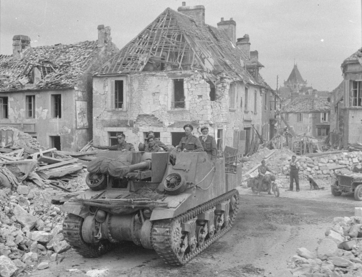 A Sexton self-propelled gun drives through the shattered village of Putanges, 20 August 1944.