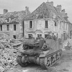 A Sexton self-propelled gun drives through the shattered village of (…)