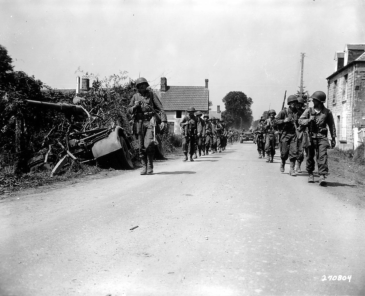 Deux colonnes de soldats américains marchent de chaque côté de la route, secteur de Folligny 31 juillet 1944