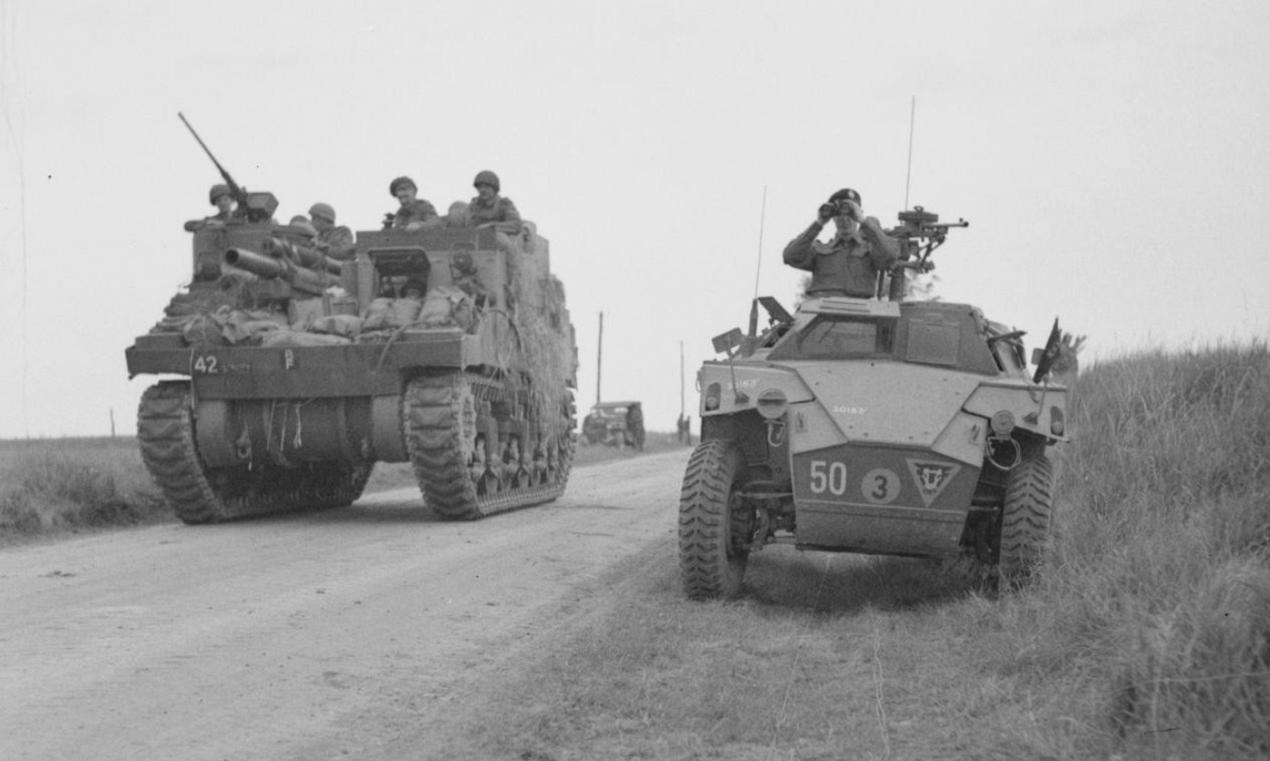 M7 Priest (left) passes a Humber scout car of 79th Armoured Division, during Operation 'Charnwood', the attack on Caen, 8 July 1944.