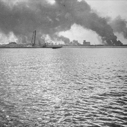 A distant view of Dunkirk harbour from a ship offshore, with smoke rising (…)