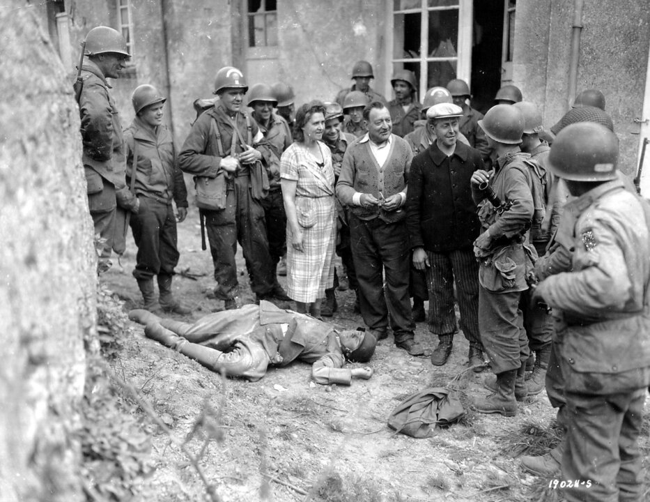 Trois civils sympathisent avec des troupes américaines, un cadavre d'officier allemand à leurs pieds