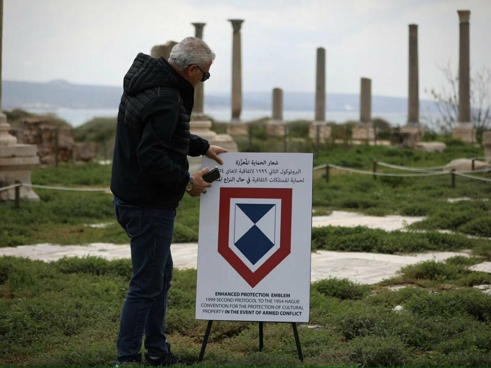 Nader Siklaoui, directeur des fouilles archéologiques au Liban-Sud pour le ministère de la Culture, plante un panneau avec le « bouclier bleu » de l'Unesco, le 23 mars 2026, entre les ruines historiques de Tyr. Photo Matthieu Karam/L'Orient-Le Jour